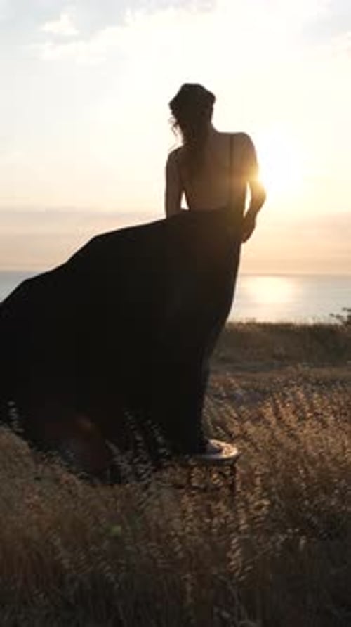 Woman Dress Sunset Elegant Woman in Flowing Black Dress on Hill Overlooking Sea at Golden Hour