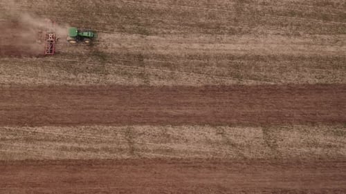 Aerial top view of tractor cutting furrows in farm field for sowing farm tractor with rotary harrow