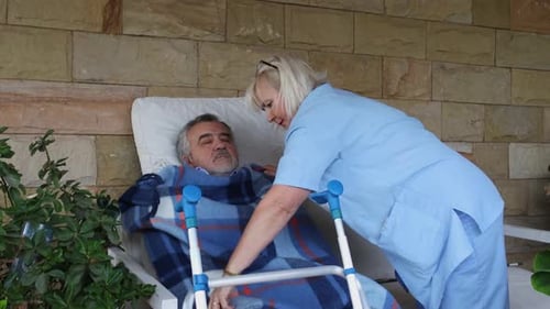 Caregiver Blankets Senior Man Relaxing in Chair