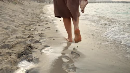 Closeup of barefoot woman walking on the wet sand and sea waves at the sandy beach on sunset