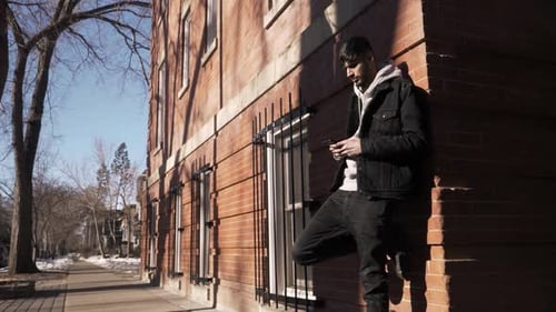 Young asian man reads text message on smart phone outside urban building
