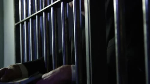 White collar crime - tilt down from face to cash through prison cell bars HD