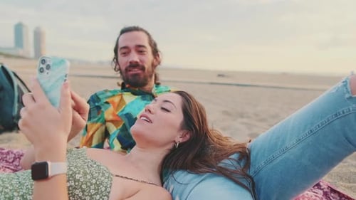 Young couple relaxing on the beach, talking, using mobile phone