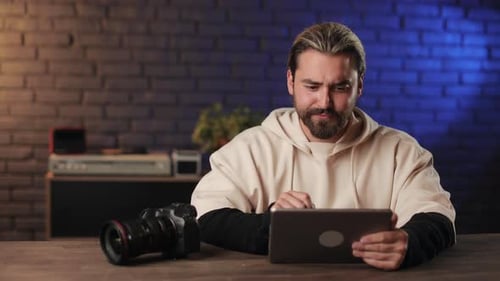 Mann sitzt am Schreibtisch mit digitalem Tablet und Fotokamera