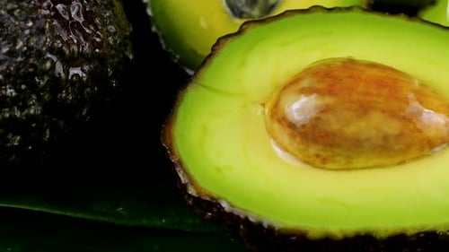 Drops of water fall on avocado fruits with leaves on a black background. Raw Fruits, healthy food.