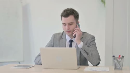 Man Using Phone and Laptop in Office