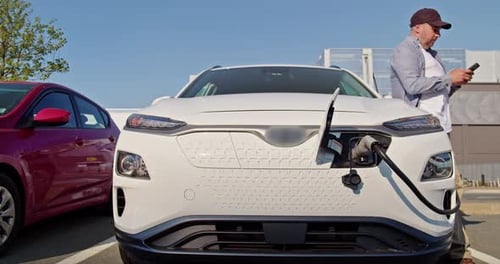 Man Charges an Electric Car at an Electric Charging Station in the City