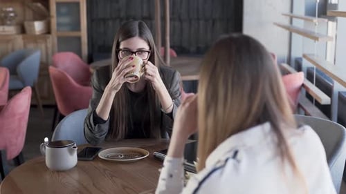 Zwei schöne junge Frauen sitzen in einem Café, trinken einen Tee und unterhalten sich. Frauen lächeln, schau