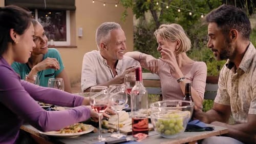 Group of Friends Gathered Around a Table in a Garden on a Summer Afternoon to Share a Meal and Have