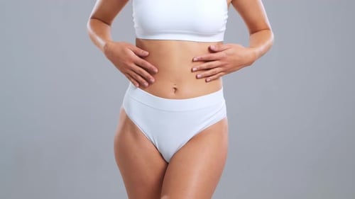 Jeune femme blonde en forme et belle en maillot de bain blanc posant sur fond gris Healthcare Diet