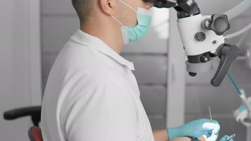 In a Contemporary Dental Clinic a Dentist Carefully Examines a Patient Using a Microscope for