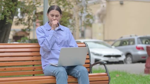 Woman Coughing While Working on Laptop on Park Bench