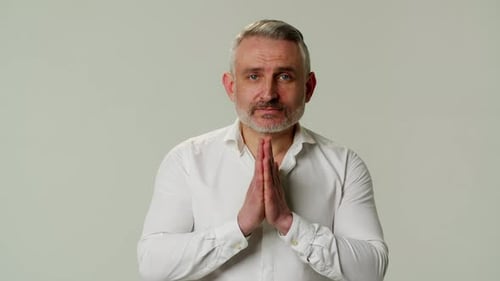Mature Man Clasping Hands Together and Looking Sincere