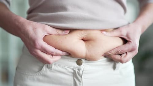 Close up of woman hands holding her belly fat. Overweight middle aged female with excess weight look