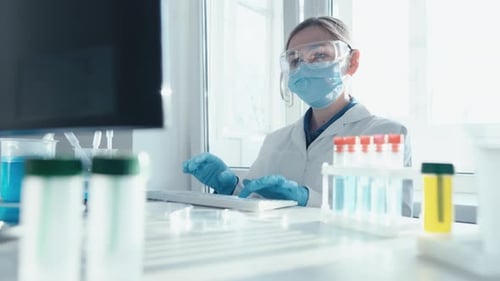 A Female Researcher Sits at a Workplace in a Laboratory Behind a Personal Computer Monitor