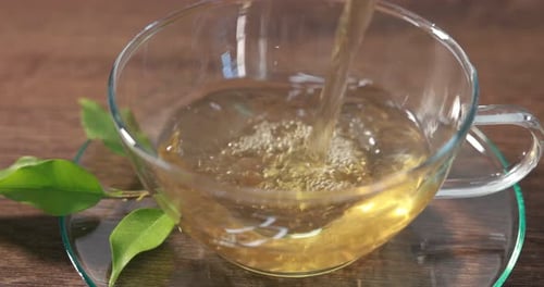 Woman pouring tasty green tea into cup and adding lemon at table, closeup