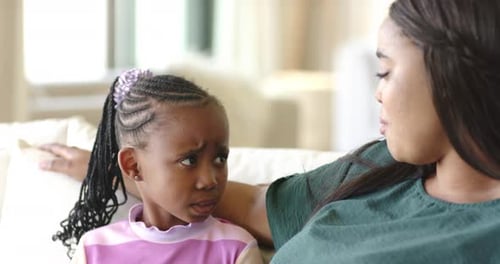 Diverse family mother clarifying confusion with daughter on light sofa as father joining smiling