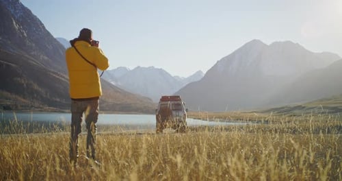 Photographer Taking Pictures By Mountain Lake with SUV in Alpine Valley