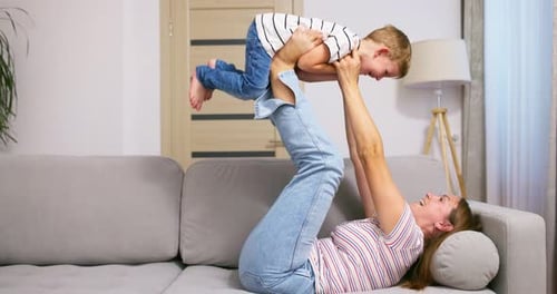 Woman Lifts Boy with Feet in Living Room