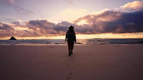 Silhouette of a Girl in a Hat with a Backpack at Sunset Near the Beach By the Ocean