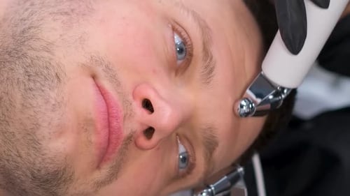 Eine Kosmetikerin führt mit modernen Geräten eine verjüngende Massage im Gesicht eines Mannes durch Vertikales Video