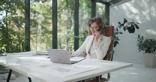 A Young Woman Architect Working with Invoices and Talking on the Phone at Her Work Office