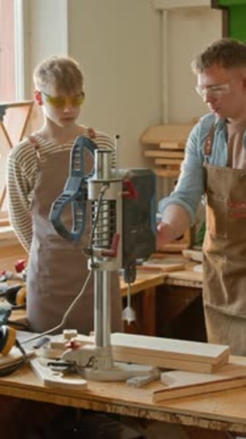 Vertical of Gen Z Woodworker Teaching Teenage Boy to Operate Drilling Machine