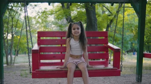 Un enfant joyeux dans une balançoire rouge aux couleurs vives appréciant le temps de jeu dans un parc serein entouré