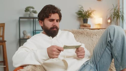 Man Sitting on Couch Counting Dollar Bills