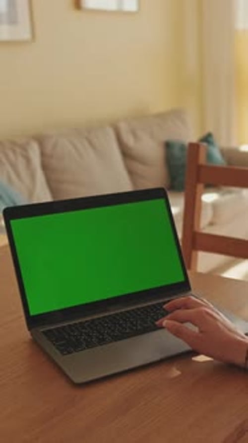 Young woman working on green screen laptop while sitting in apartment
