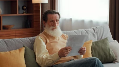 Senior Man Reading a Letter While Sitting on a Couch in a Cozy Living Room