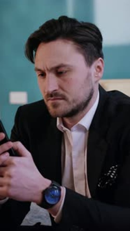 Ein professioneller Mann in einem eleganten Anzug nutzt sein Smartphone aktiv für Arbeitszwecke