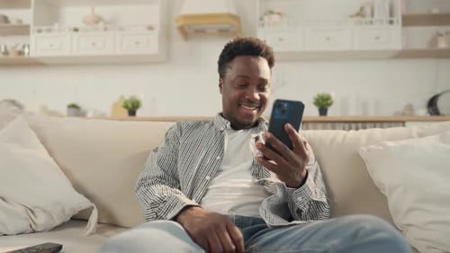 Smiling Man Using Smartphone on Comfortable Sofa