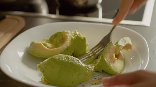 Person mashing ripe avocados with fork in kitchen
