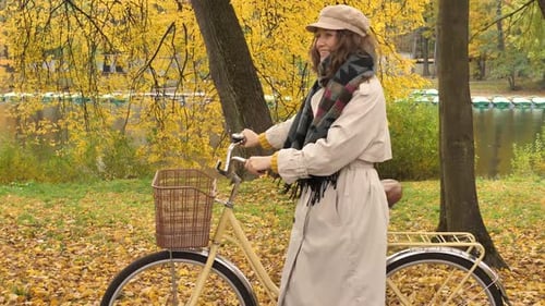 Nice Smiling Woman Walking with a City Bike in the Autumn Park Along the Lake