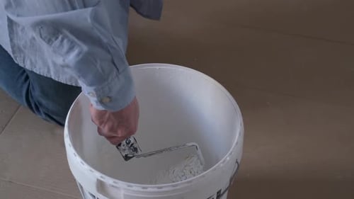 Close up of professional workman soaking paint roller into white paint bucket.