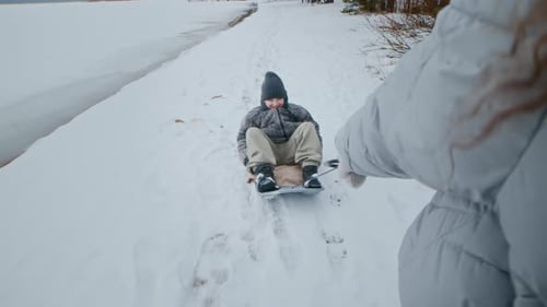 Mother Pulling Son on Sled along Snowy Winter Path