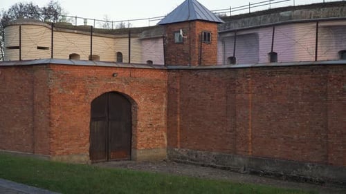 view of jail prison dark red brick wall with a barbed wire fence on top and turrets in the corners