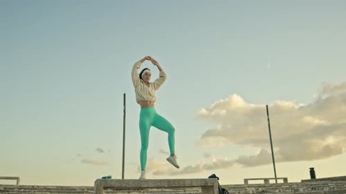 Young Woman Stretching on Concrete Structure Under Blue Sky
