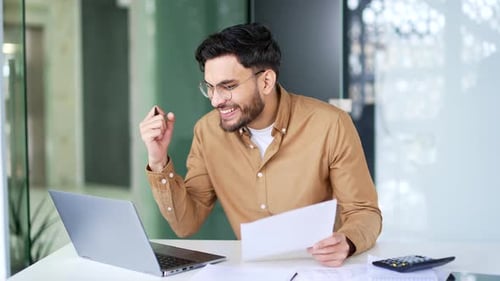 Happy financier is satisfied with results of financial report he is reviewing sitting at workplace