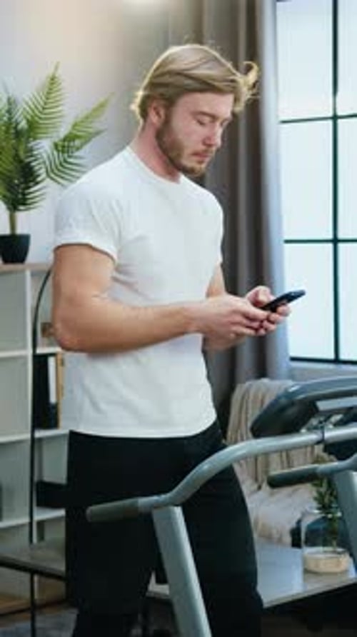 Young Man Using Phone Next to Treadmill