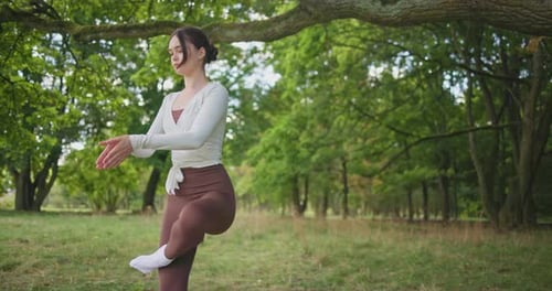 Young Beautiful Athletic Woman in Sportswear Doing Stretching and Warming Up in the Park Near a Tree