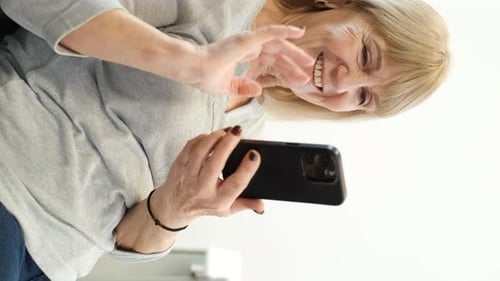 Une femme retraitée d'apparence européenne parle à l'interphone à l'aide d'un smartphone moderne