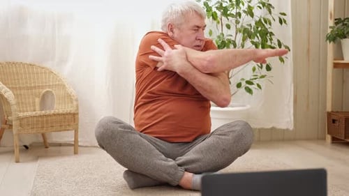 Feliz hombre mayor maduro haciendo ejercicios de gimnasia en casa en línea con una computadora portátil, estilo de vida saludable