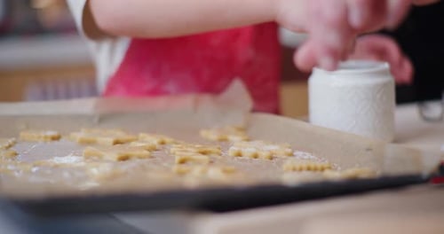 Nahaufnahme einer Jungenhand, die Zucker auf Kekse streut