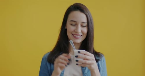 Young Woman Eating Yogurt Against Yellow Background
