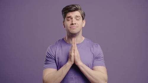 Man Prays with Hands Together Against Purple Background