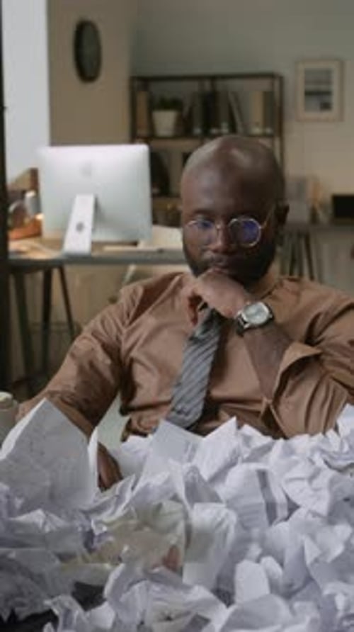 Stressed Office Worker Rubbing Eyes Among Paper Mess