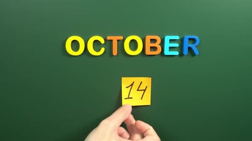 Hand sticking a sticker 14 October calendar day on school board. 14 date of October. Fourteenth