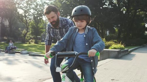 Man Teaching Boy How to Ride Bike in Park